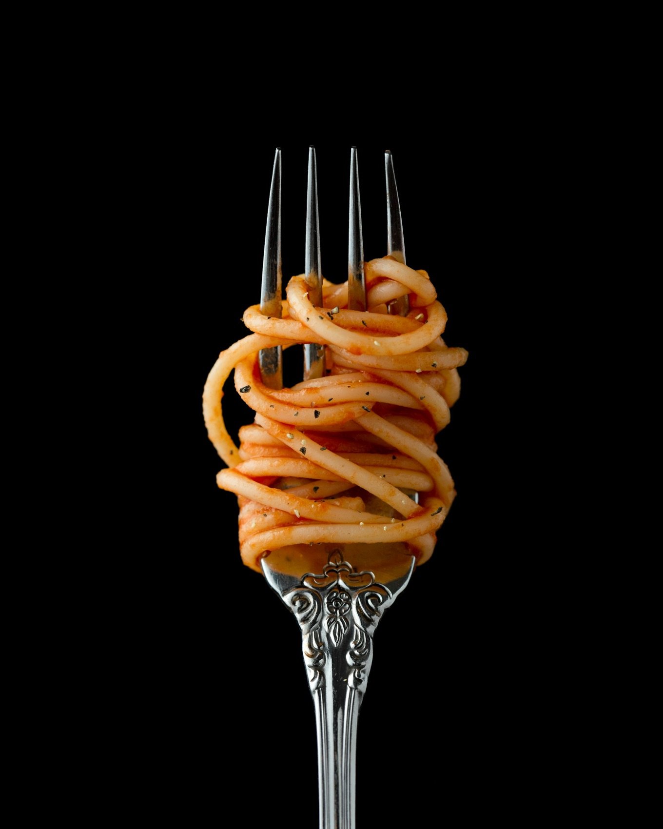 Tenedor con spaghetti enrollado en salsa de tomate sobre fondo negro